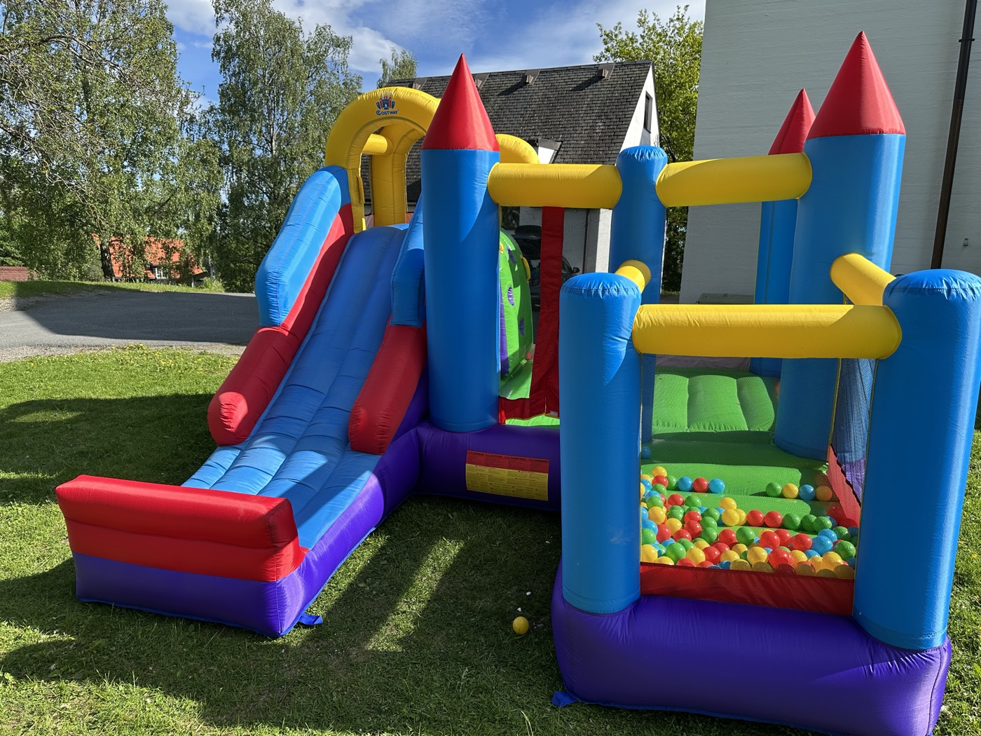 Hoppeslottet med sklie og basketkurv, oppblåst på en plen en solrik dag